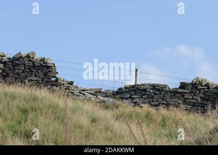 Profile of drystone wall and barbed wire fence against pastel blue sky background. Autumn rural season in the peak district, selective focus texture. Stock Photo