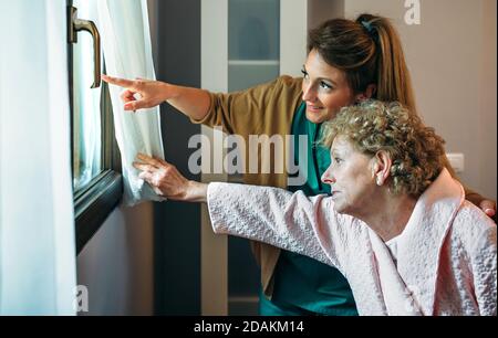 Caregiver showing the view through the window to elderly patient Stock Photo