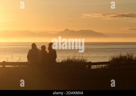 Croy Shore , Ayrshire, Scotland UK. People enjoying sunset over Arran, with a seamist Haar on the horizon with Isle of Arran behind Stock Photo