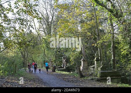 Dog walkers and runners in Nunhead Cemetery, south London, UK. An impressive Victorian cemetery now wild and overgrown, but popular with local people. Stock Photo