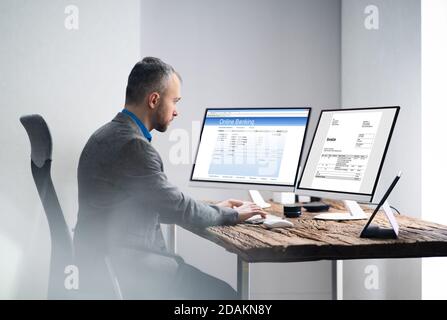 Young Businessman Looking At Invoice While Doing Online Banking On Computer Stock Photo
