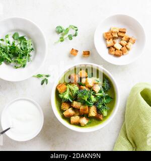 Healthy broccoli green pea cream soup with croutons in bowl over light stone background. Diet detox food concept. Top view, flat lay Stock Photo