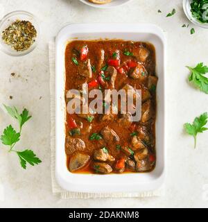 Close up view of peri-peri chicken livers in baking dish over light stone background. Stewed chicken liver with vegetables in tomato sauce. Top view, Stock Photo