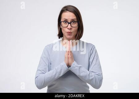 Mature woman wearing glasses keeps palms together, has pleased expression Stock Photo