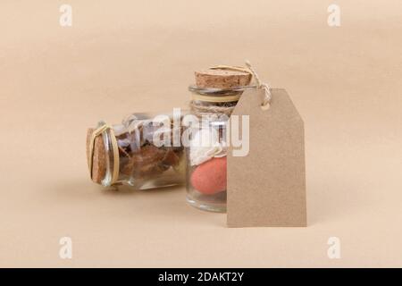 Two glass jars with dried herbs for aromatherapy with empty rectungolar tag on craft paper backrgound. Side view of dry perfume jar with various dried Stock Photo