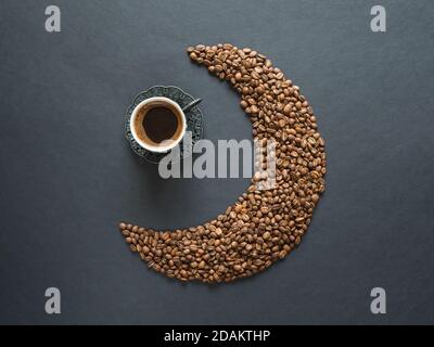 Crescent shape made of coffee beans and a cup of black coffee on black background. Top view. Stock Photo