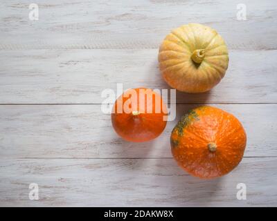 Three ripe pumpkins on a white wooden background. Top view. Stock Photo