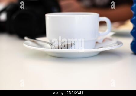 White wide ceramic old fashioned coffee mug standing a white plate with a metal spoon on it Stock Photo