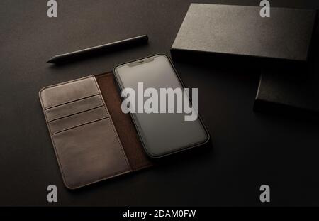 Mobile phone with case and box, leather case, soft side light on office table, elegant presentation of product with black and gray colors, ideal for m Stock Photo