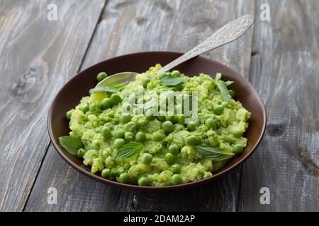 Mashed potatoes with green peas, mint and olive oil in a ceramic bowl on a wooden table. Healthy vegetarian food Stock Photo