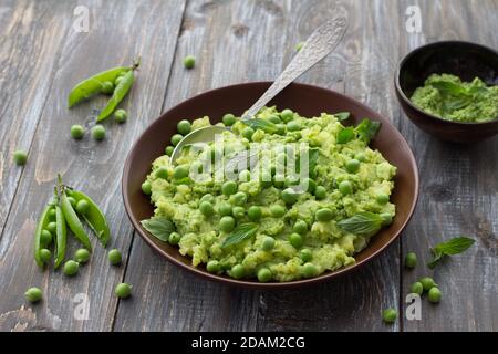 Mashed potatoes with green peas, mint and olive oil in a ceramic bowl on a wooden table. Healthy vegetarian food Stock Photo