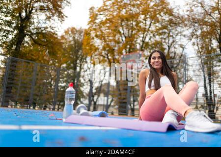 Fitness girl sitting on yoga mat on blue floor of sports ground Stock Photo