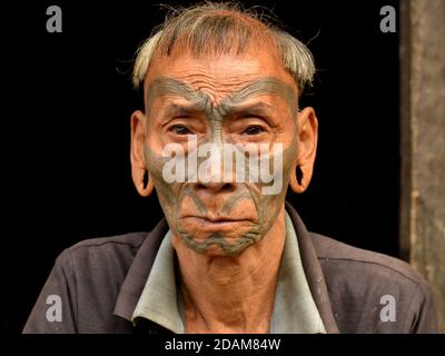 Old retired Indian Konyak Naga warrior and ex-headhunter with distinctive tribal facial tattoo and traditional hairstyle poses for the camera. Stock Photo
