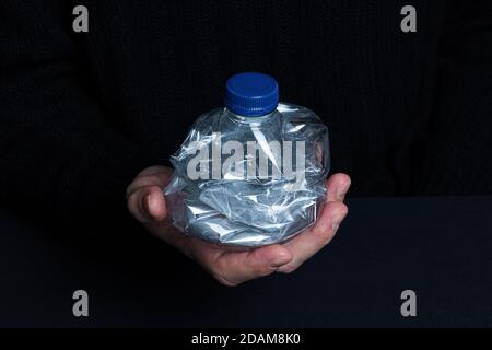 Hand holding smashed empty plastic bottle isolated on a black background Stock Photo