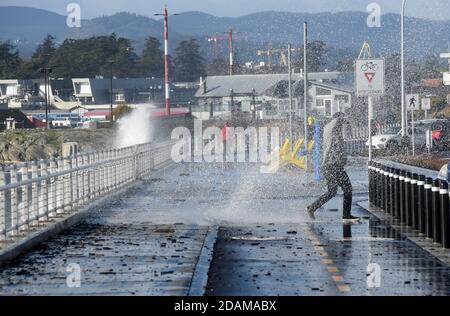 Victoria, British Columbia, Canada, 13 Nov 2020 - A pedestrian is soaked as huge waves break against the shoreline along Dallas Road in Victoria after high winds hit Vancouver Island causing power outages throughout the area.  Don Denton/Alamy Live News Stock Photo