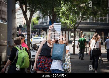 BELGRADE, SERBIA - JULY 9, 2018: Two girls standing and observing developped film negative from analog photography in the streets while holding a smar Stock Photo