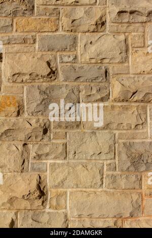 Full frame texture background of a modern beige brown natural stone wall in ashlar brickwork design, with rough cut limestone blocks Stock Photo