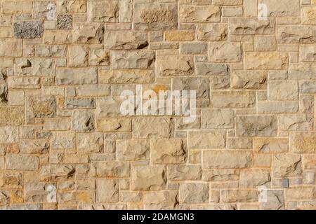 Full frame texture background of a modern beige brown natural stone wall in ashlar brickwork design, with rough cut limestone blocks Stock Photo