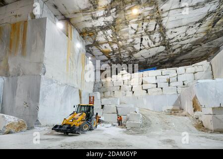 Workers and machinery inside a marble quarry or open cast mine during excavation of the white stone inside a mountain in Carrara, Tuscany, Italy Stock Photo