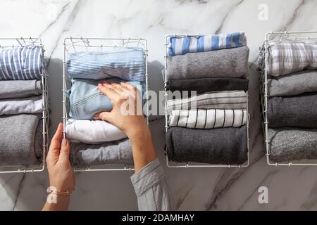 Neatly folded clothes and pyjamas in the metal mesh organizer basket on white marble table. Stock Photo