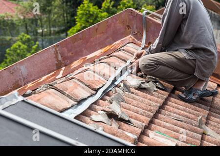 Asian worker replacing roof tiles of old residential building Stock Photo