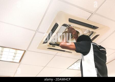 Technician servicing, maintaining and fixing a ceiling air conditioner cartridge Stock Photo
