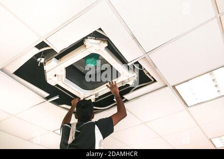 Technician servicing, maintaining and fixing a ceiling air conditioner cartridge Stock Photo
