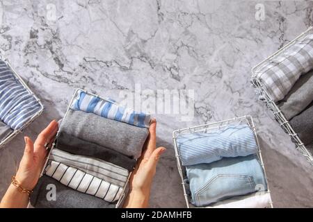 Neatly folded clothes and pyjamas in the metal mesh organizer basket on white marble table. Stock Photo