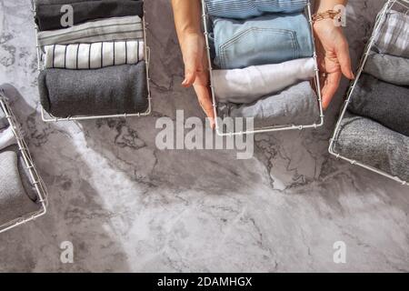 Neatly folded clothes and pyjamas in the metal mesh organizer basket on white marble table. Stock Photo