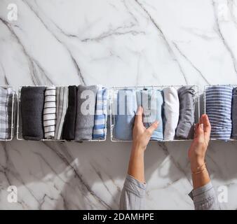 Neatly folded clothes and pyjamas in the metal mesh organizer basket on white marble table. Stock Photo