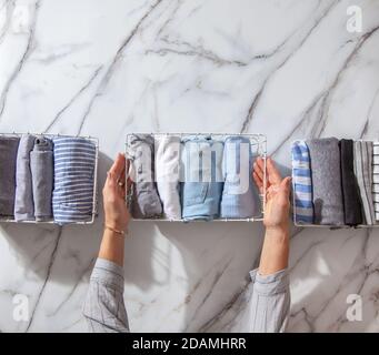 Neatly folded clothes and pyjamas in the metal mesh organizer basket on white marble table. Stock Photo