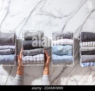 Neatly folded clothes and pyjamas in the metal mesh organizer basket on white marble table. Stock Photo