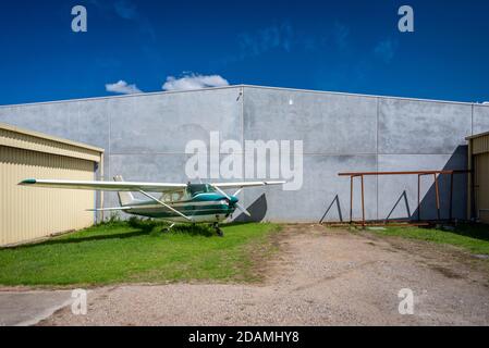 An older private aircraft appearing lonley against a concrete wall and yellow hanger against a blue sky and a few clouds Stock Photo