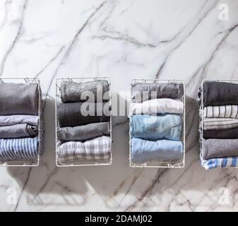 Neatly folded clothes and pyjamas in the metal mesh organizer basket on white marble table. Stock Photo