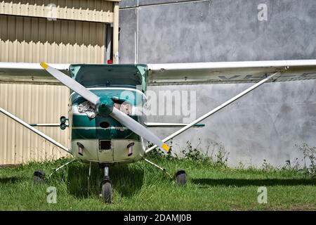 An older private aricraft against a yellow faded hanger and on overgrown grass Stock Photo