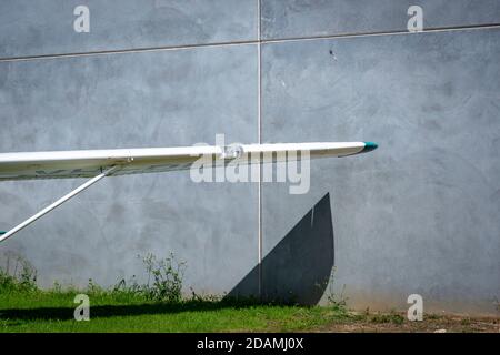 Wing of an old plane, throwing a shadow against a concrete wall and green lawn Stock Photo