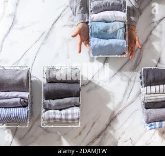 Neatly folded clothes and pyjamas in the metal mesh organizer basket on white marble table. Stock Photo