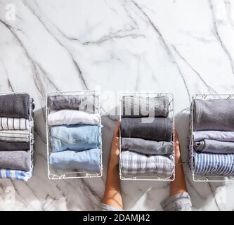 Neatly folded clothes and pyjamas in the metal mesh organizer basket on white marble table. Stock Photo