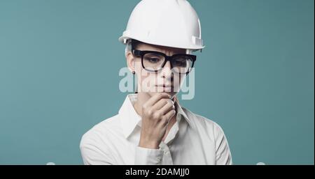 Pensive young businesswoman wearing a safety helmet and thinking with hand on chin Stock Photo