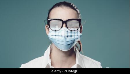Woman wearing a protective surgical mask to prevent coronavirus, her glasses are fogged up Stock Photo