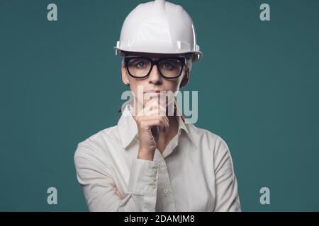 Pensive young businesswoman wearing a safety helmet and thinking with hand on chin Stock Photo