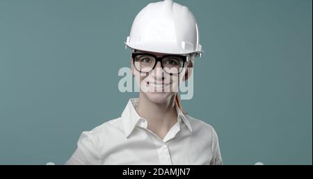 Smiling cheerful businesswoman wearing a safety helmet and looking at camera Stock Photo