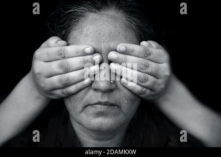 Modern creative shot of a lady with hands closing her lips and expressing see no evil isolated on black background in black and white colors. Stock Photo