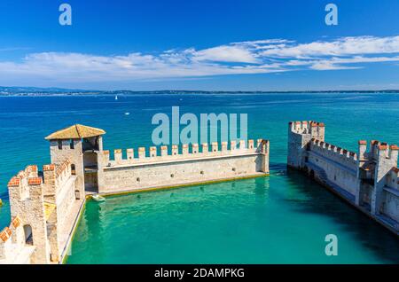 Sirmione, Italy, September 11, 2019: Small fortified harbor with turquoise water, Scaligero Castle Castello fortress, town on Garda lake, medieval castle with stone towers and brick walls, Lombardy Stock Photo