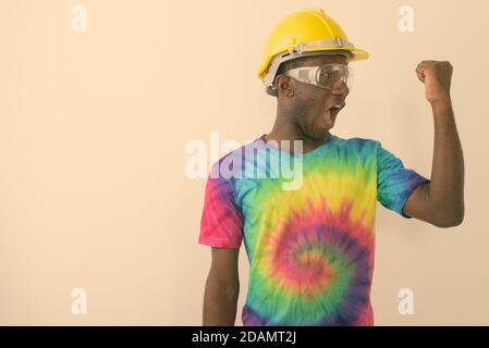 Studio shot of young black African man construction worker wearing hard hat and safety glasses while flexing his bicep against white background Stock Photo