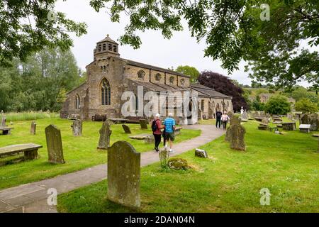 Historic scenic St Michael & All Angels Church exterior & people walking on churchyard pathway to entrance porch - Linton, Yorkshire Dales, England UK Stock Photo