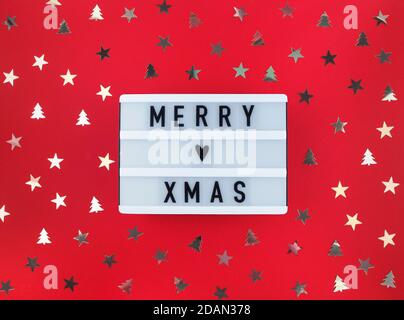 Merry Xmas greeting on light box and confetti on a red background. Stock Photo