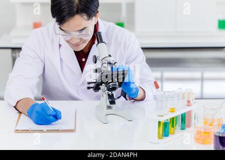 Asian male scientist working at laboratory desk with medical sample  record and microscope science equipment. Stock Photo