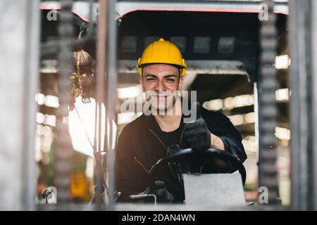 Caucasian russian worker happy smiling and driving forklift car in cargo logistic shipping industry factory or warehouse. Stock Photo