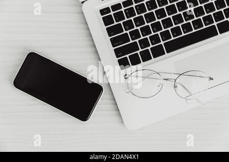laptop computer on the desk with smartphone and glasses top view monotone for minimal business flat lay picture. Stock Photo